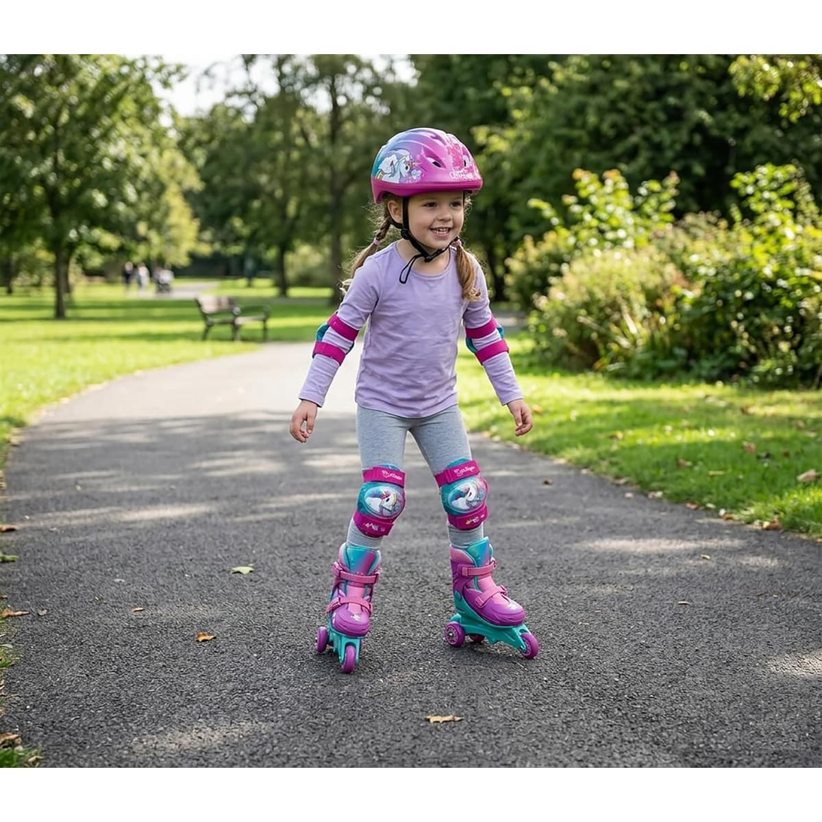 Bambina sorridente che pattina sul vialetto del parco con i pattini Mondo Be Unique Unicorno tri-inline, casco e protezioni ginocchia abbinati