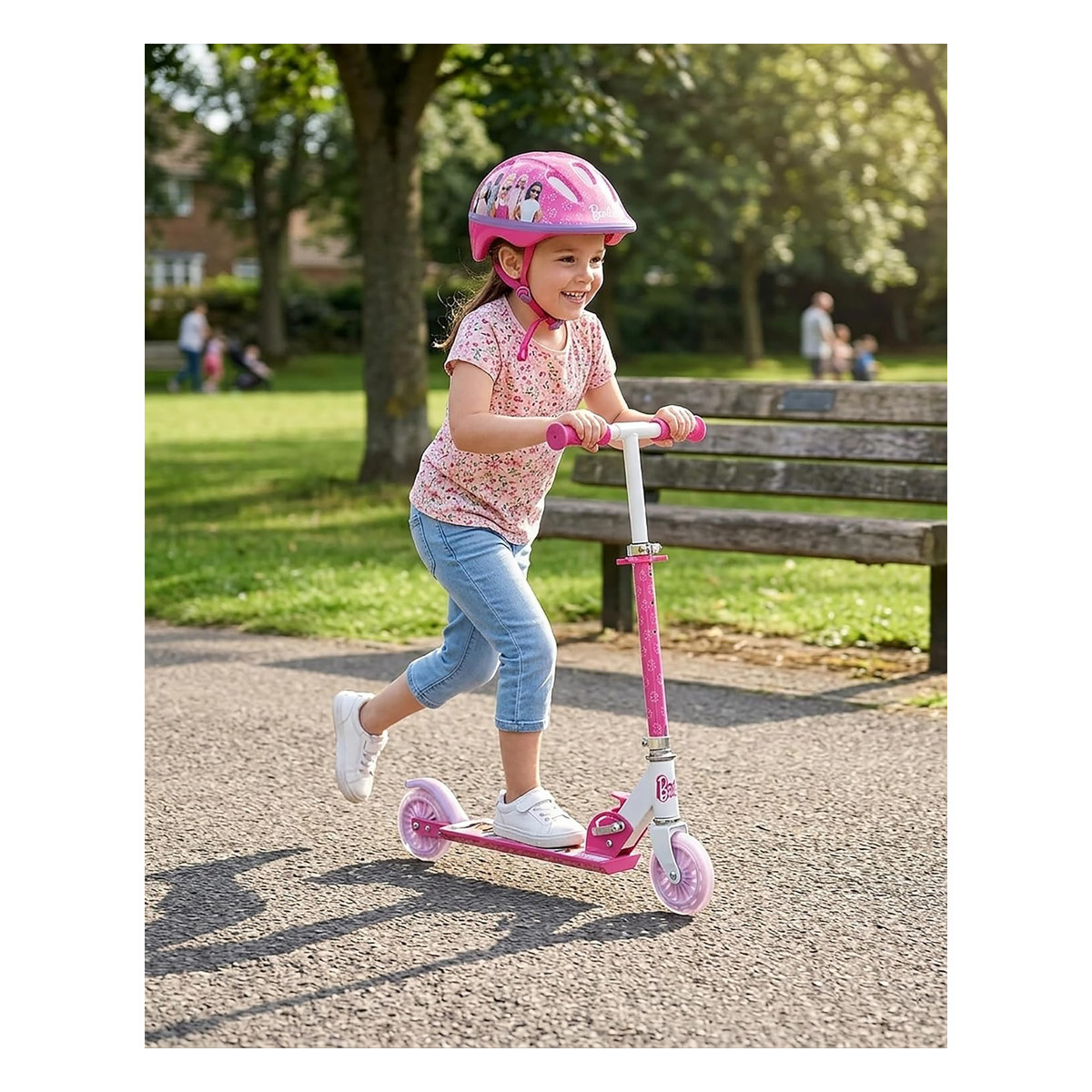 Bambina con casco rosa guida il monopattino su un vialetto del parco tra gli alberi