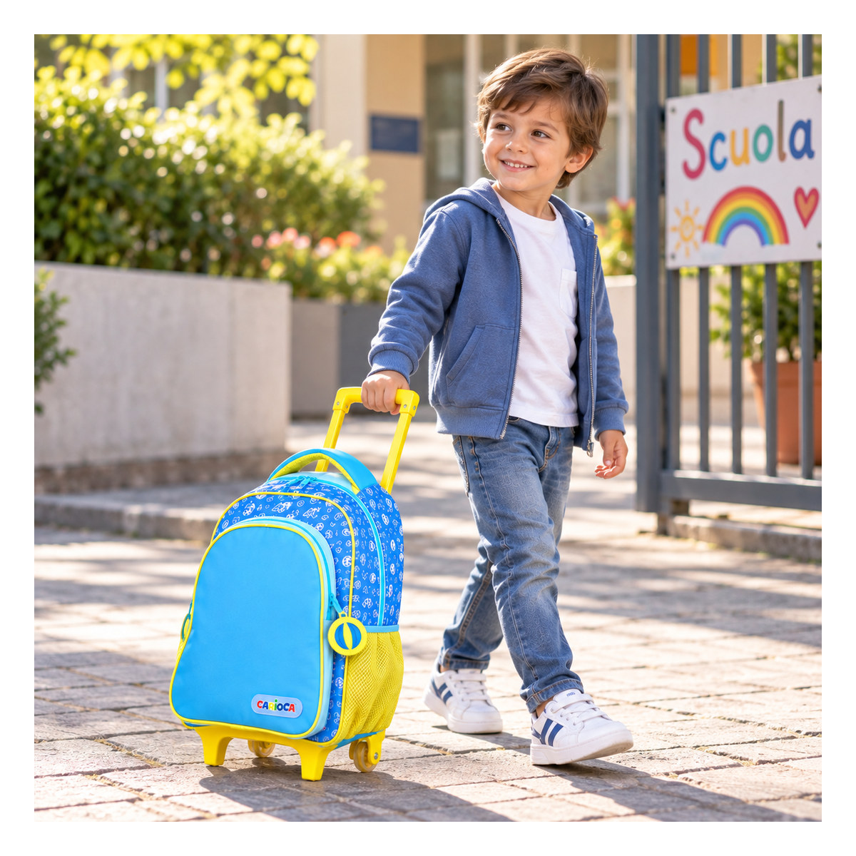 Bambino con felpa blu tira lo zaino trolley per la maniglia davanti al cancello della scuola
